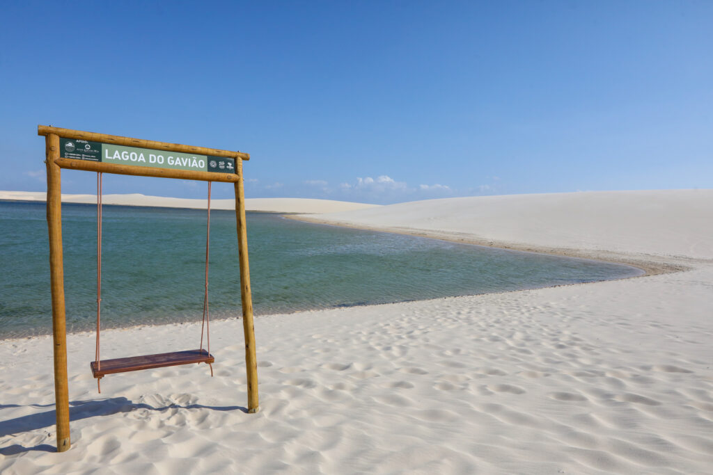 Balanço de madeira na Lagoa do Gavião cercado por dunas brancas nos Lençóis Maranhenses.