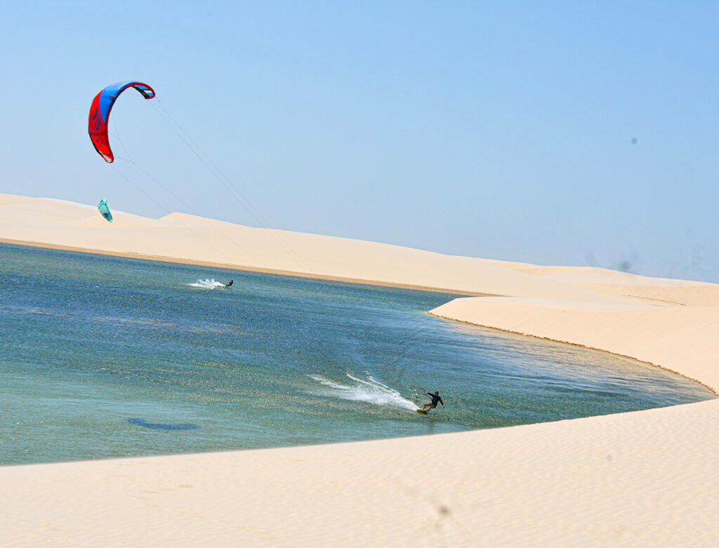 Kitesurfista velejando em uma lagoa de águas cristalinas cercada por dunas brancas nos Lençóis Maranhenses, Atins.
