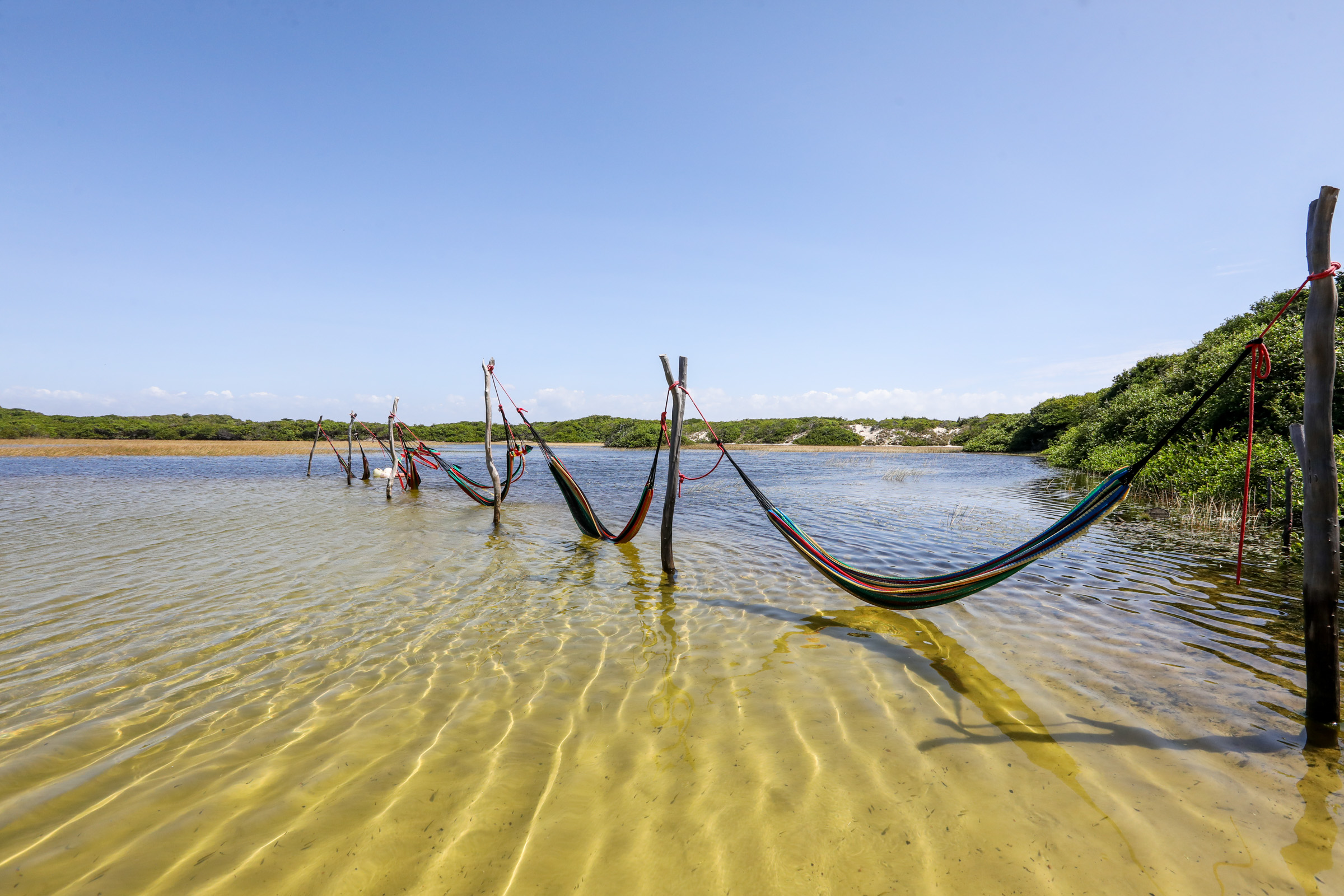 Colorful hammocks installed in the water of a shallow, crystal-clear lagoon in Lençóis Maranhenses.