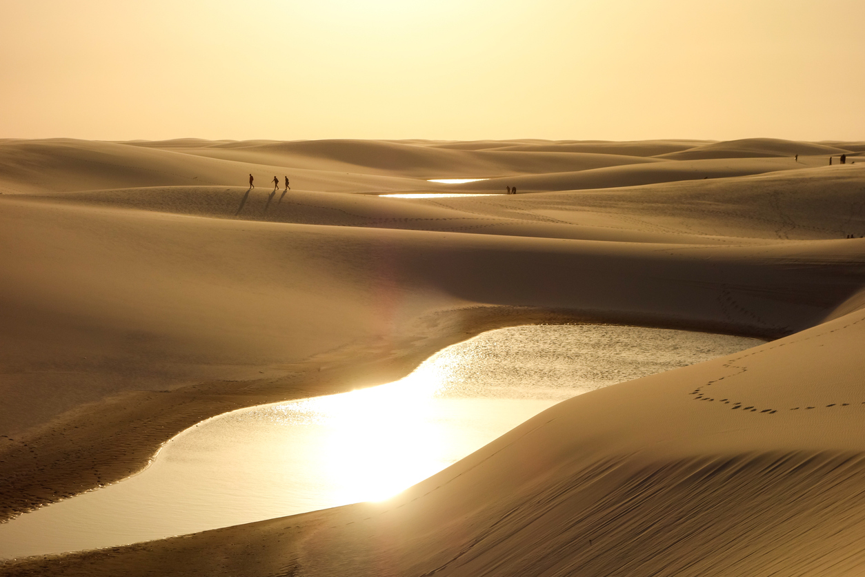 People walking along the top of the dunes at sunset with the reflection of golden light on the lagoons of Lençóis Maranhenses.