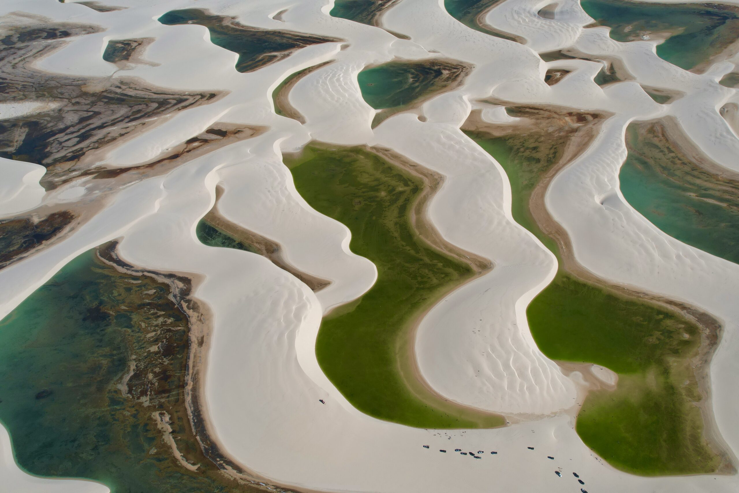 Aerial view of the white sand dunes and crystal-clear green water lagoons in Lençóis Maranhenses National Park.