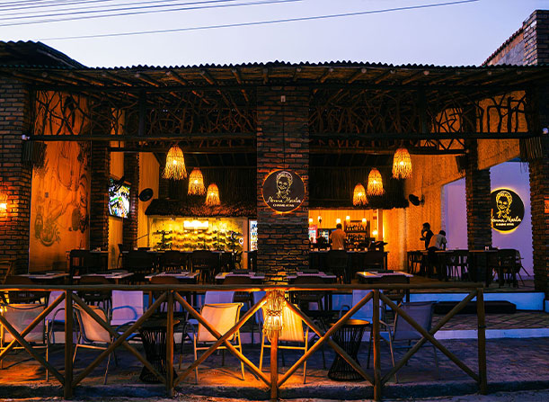 Entrada nocturna al restaurante Nonna Marta en Atins, Maranhão, con iluminación cálida y estilo arquitectónico local, parte de Charme Atins.