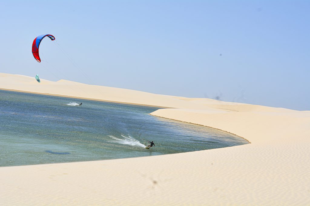 Kitesurfistas deslizando em lagoa cercada por dunas de areia em Atins.