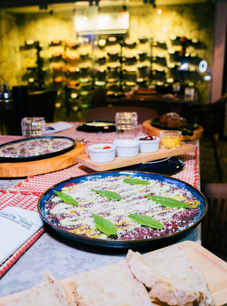 Entrada de carpaccio com torrada artesanal e adega ao fundo no Restaurante Nonna Marta em Atins.