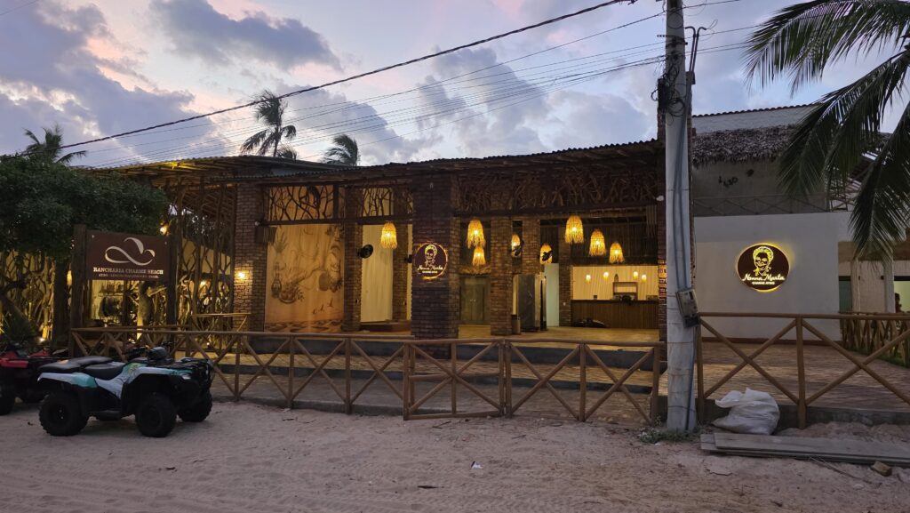 Fachada exterior de la pizzería Nonna Marta Charme Atins durante la noche, una construcción de madera iluminada con luces cálidas, con un área de asientos al aire libre y un cuatriciclo estacionado cerca de la entrada.