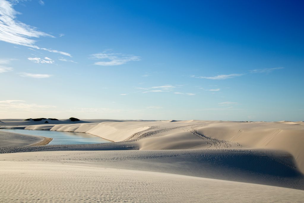 Extensão de dunas de areia branca e lagoa cristalina sob céu azul em Atins.
