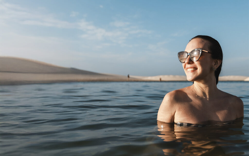 Mulher sorrindo em banho de lagoa com dunas ao fundo em Atins.