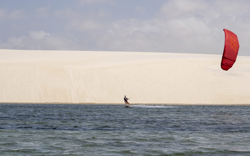 Kitesurfista velejando com pipa vermelha em frente às dunas de Atins.